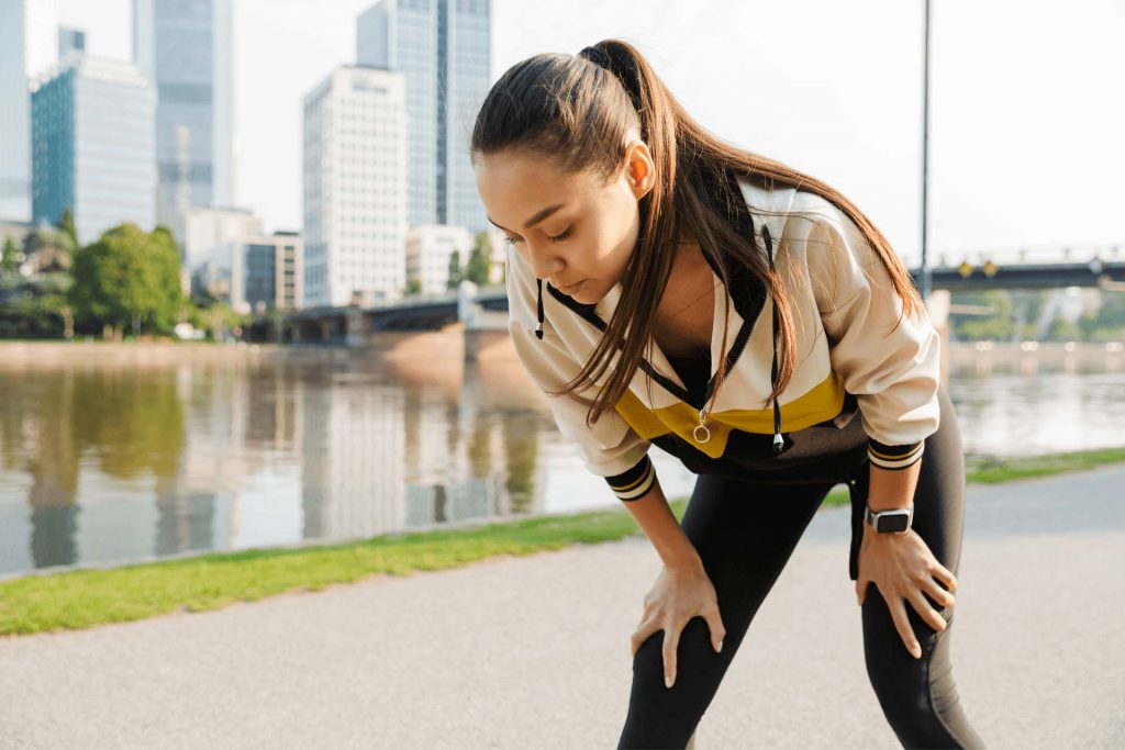 Photo of concentrated caucasian woman in sportswear resting while working out near city river
